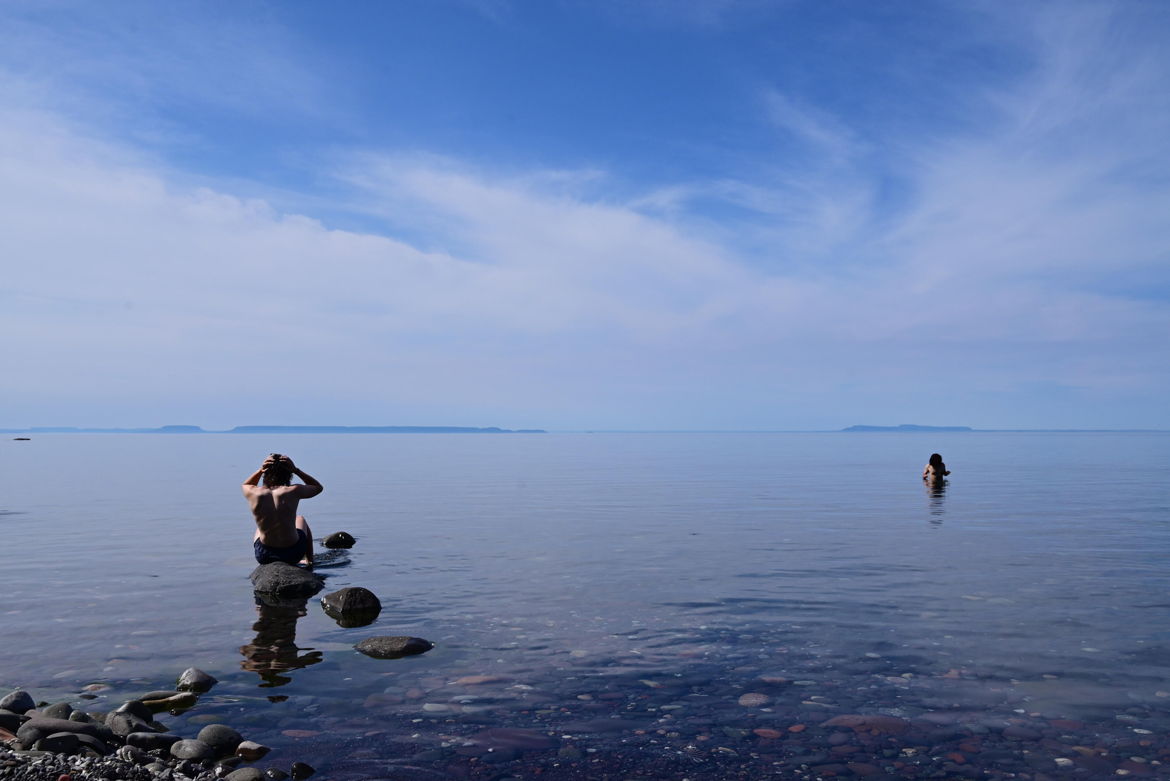 Lake Superior Swimming Two backpackers swim in calm, glass like, water in Lake Superior with only rocks in and under the water and the distant Canadian shore visible